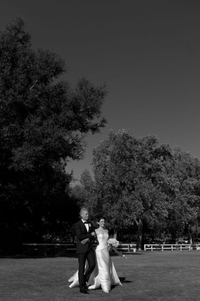 Bride comes down the aisle with her father in an outdoor wedding ceremony.