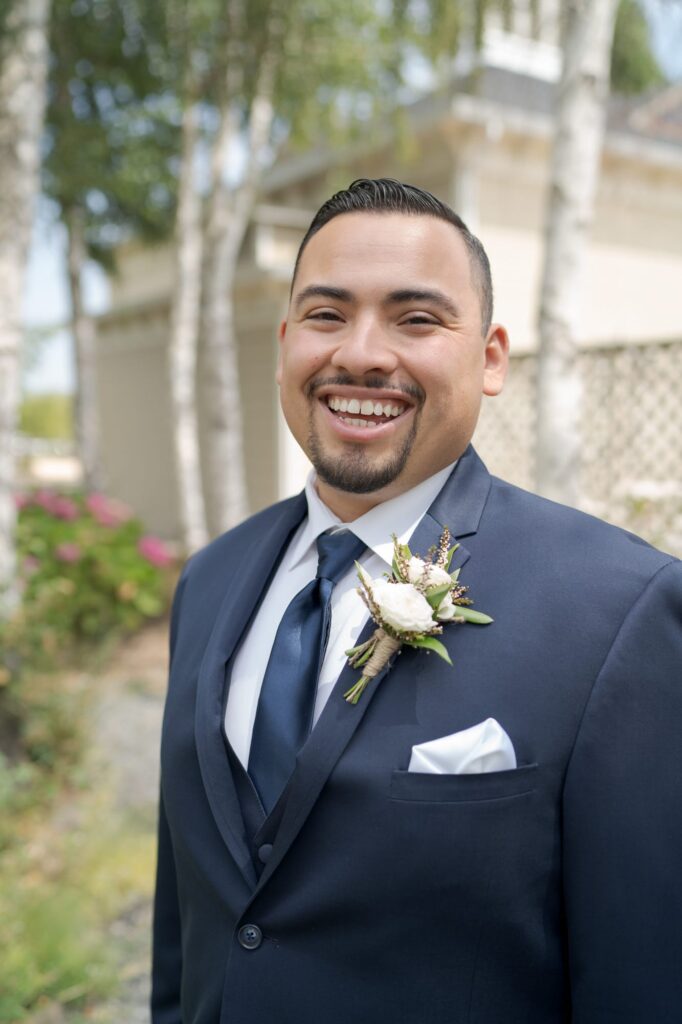 Bridegroom wears a blue suit jacket with white boutonnière flowers and a white lapel sticking out from the pocket.