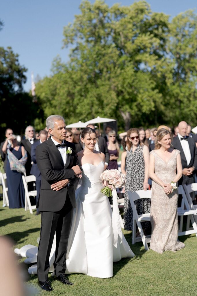 Father of the bride helps his daughter walk down the aisle.