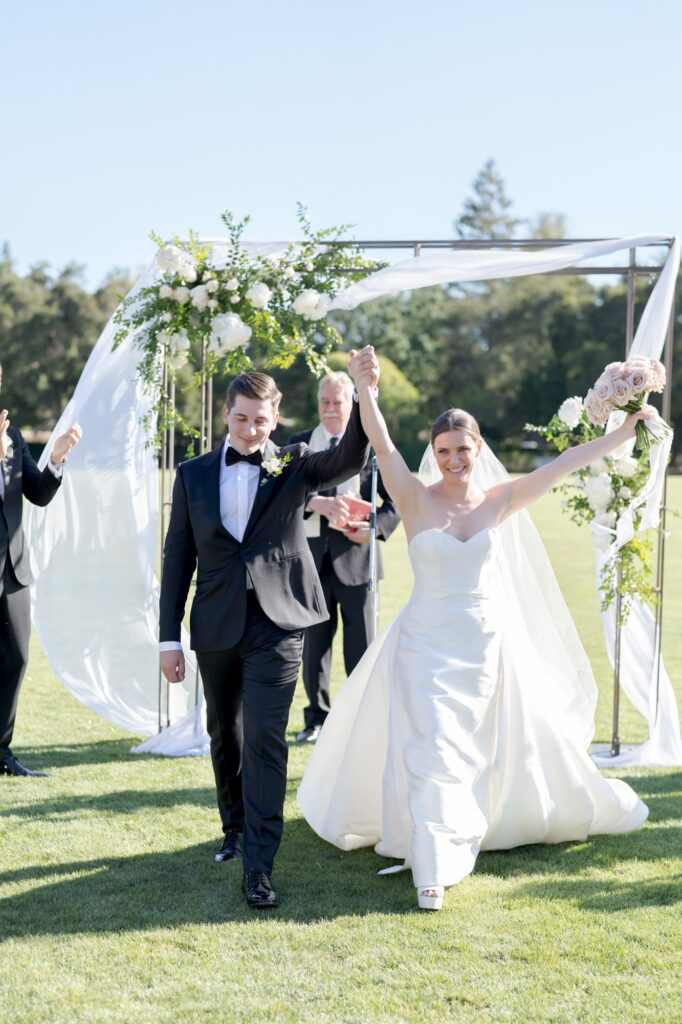 Bride and groom raise hands in celebration and walk back up the aisle.