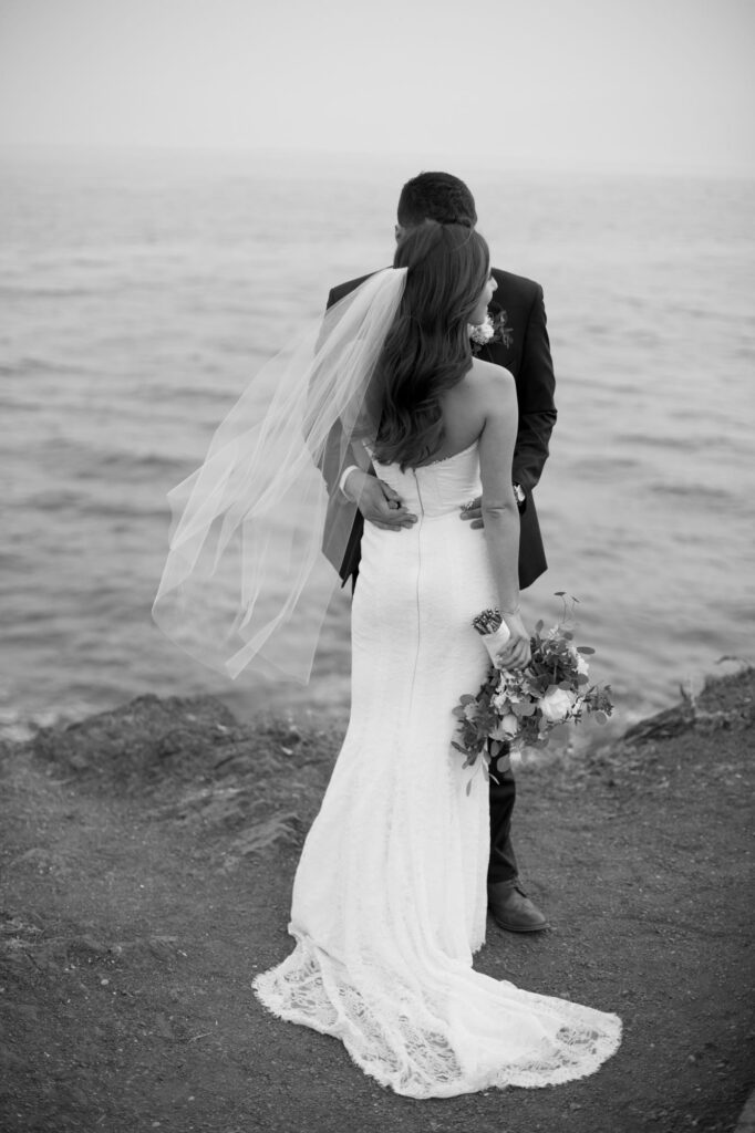 Husband in wedding suit embraces his wife in a white wedding gown.