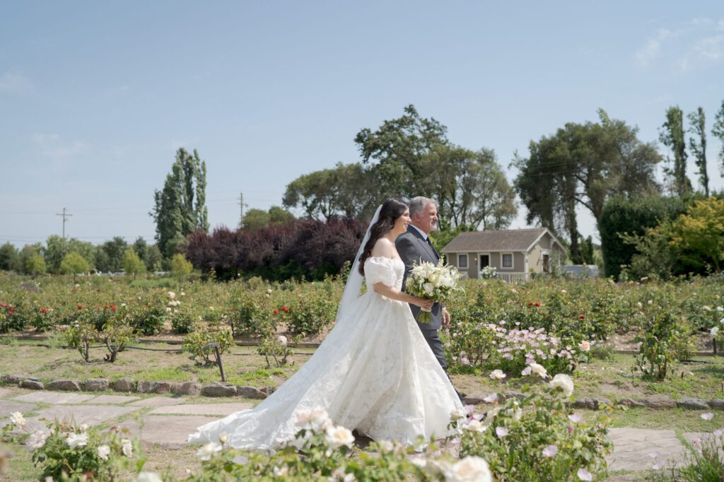 Father of the bride walks his daughter down the outdoor wedding aisle.