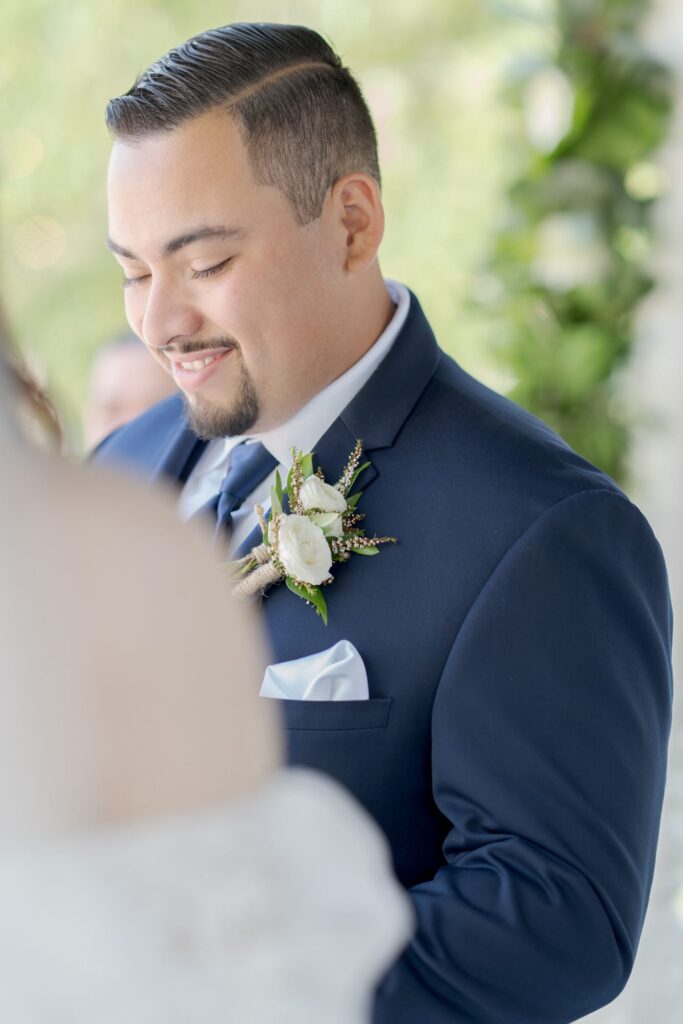 Bridegroom dressed in a blue suit and tie attends his wedding officiation ceremony.