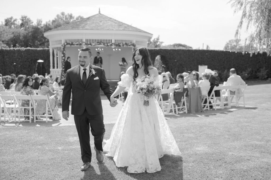 Bride and groom hold hands and walk back up the aisle at their beautiful outdoor wedding officiation ceremony venue.