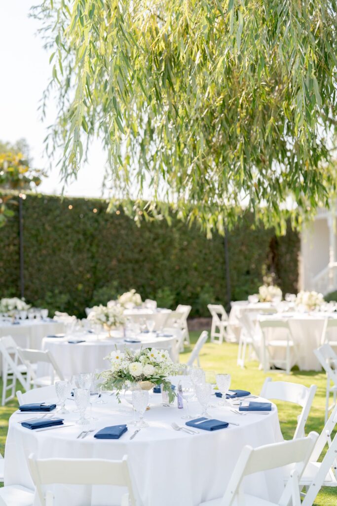 Outdoor wedding reception party venue with beautifully arranged white dining tables and chairs.