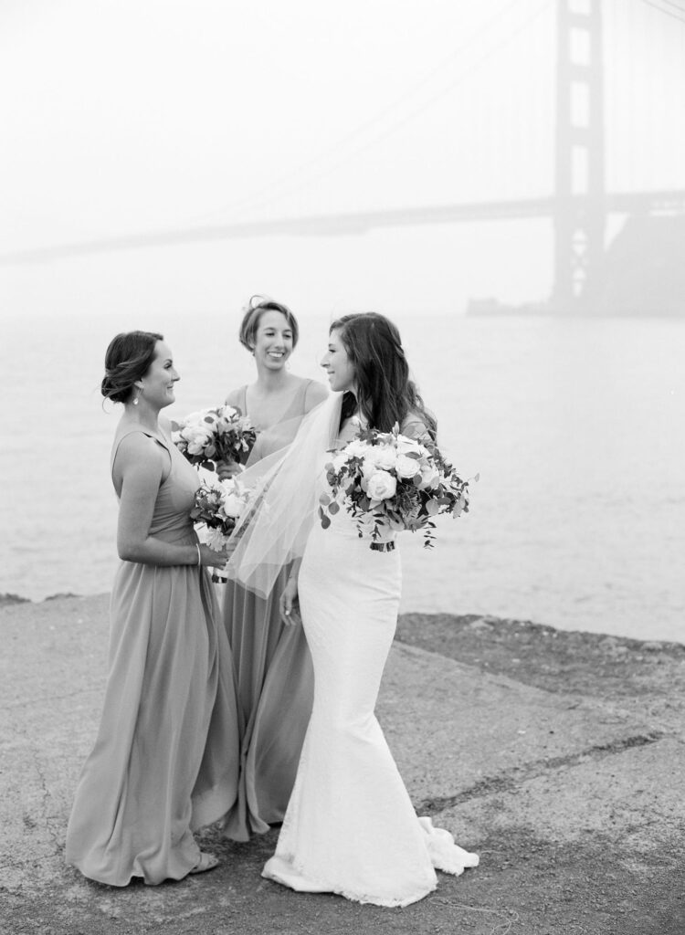 Bride and her bridesmaids hold flower bouquets in front of the Golden Gate Bridge.