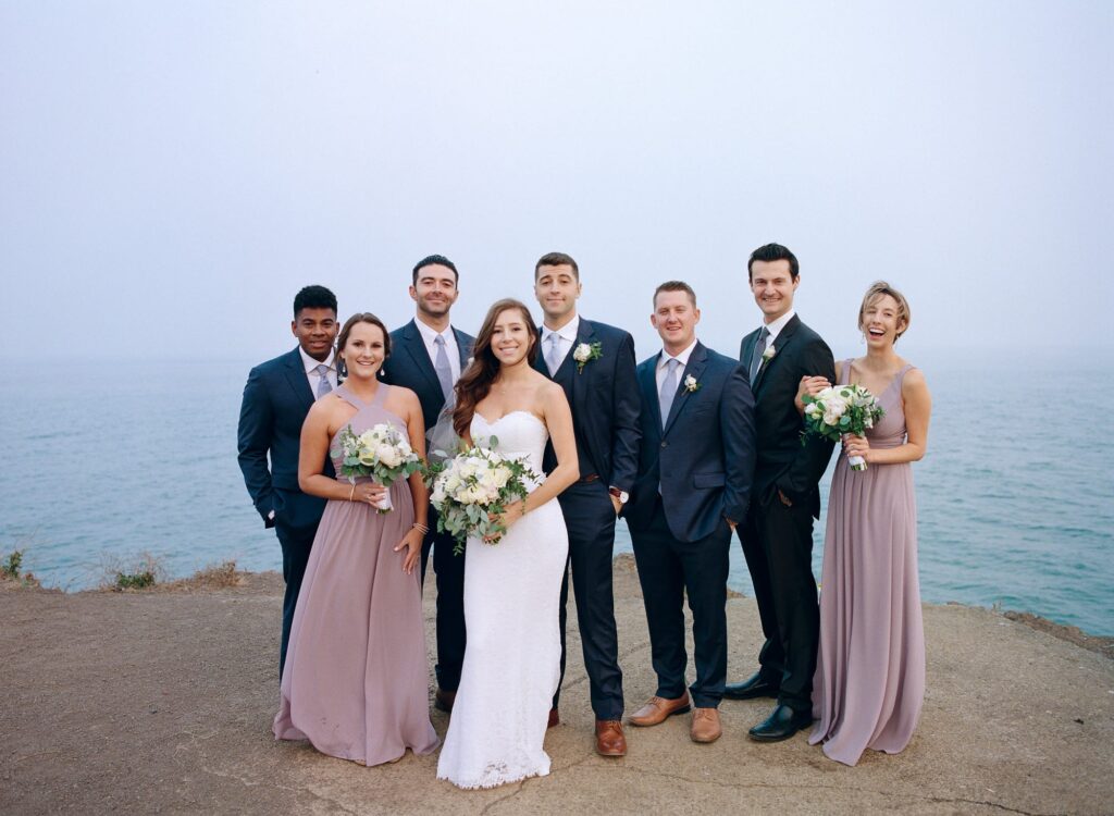 Ocean-side wedding photoshoot of the bride, groom, best men, and bridesmaids.