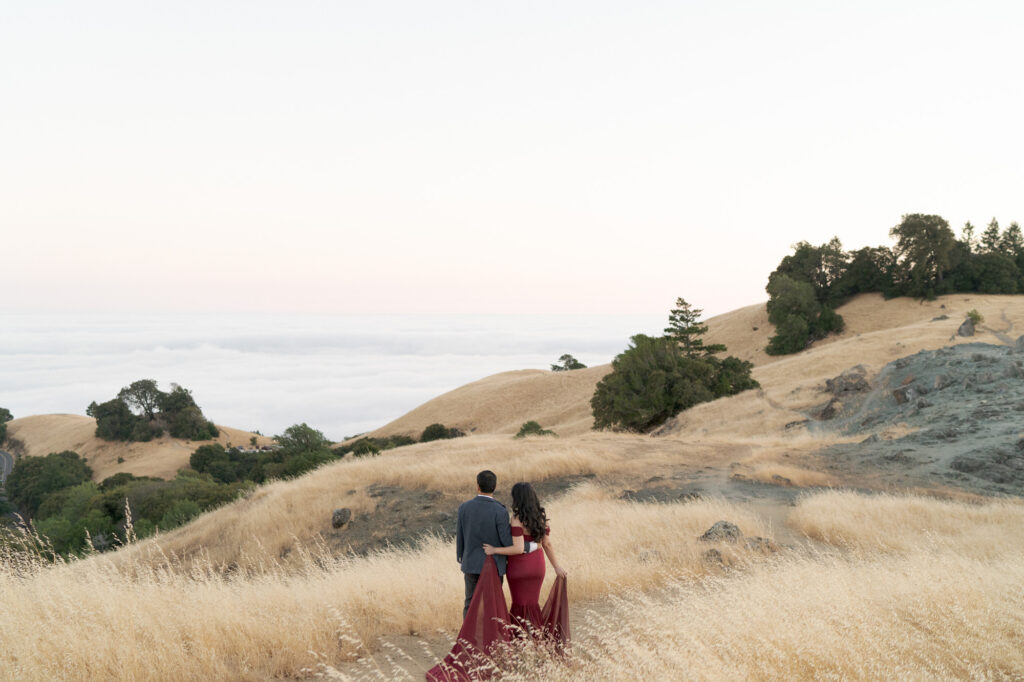 Loving couple embrace each other and look into the distant sea of clouds beneath them.