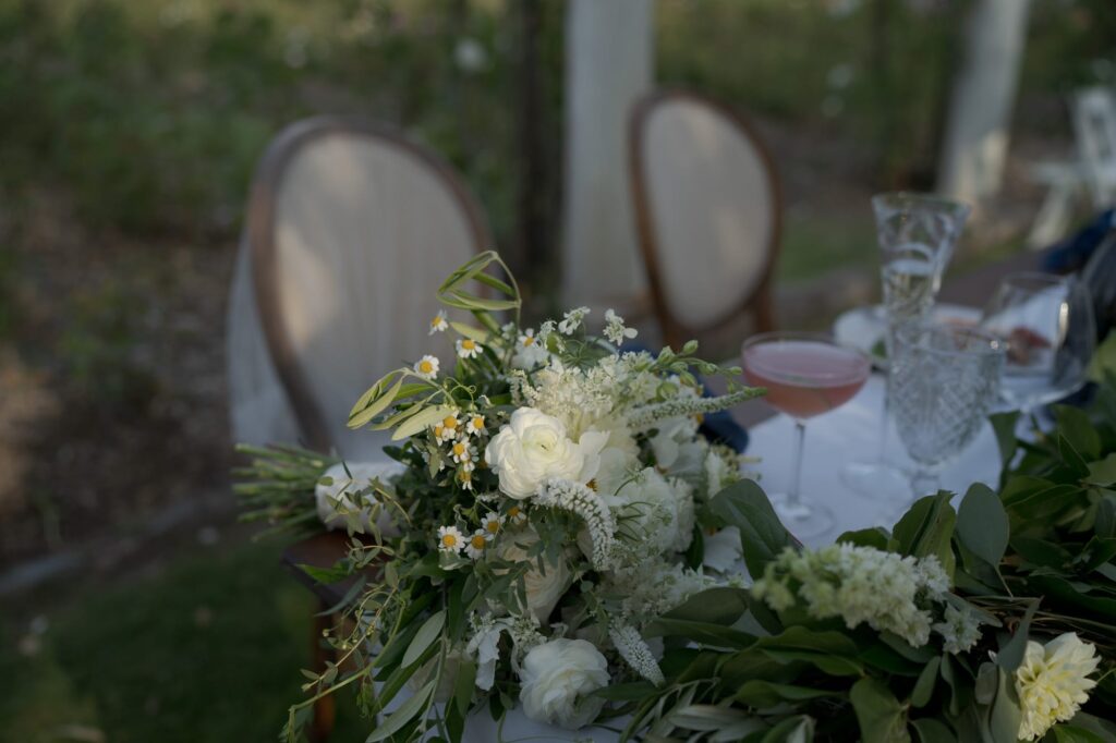 Beautiful flower and leaf bouquet in front of the bride and groom's table with drinks and chairs.