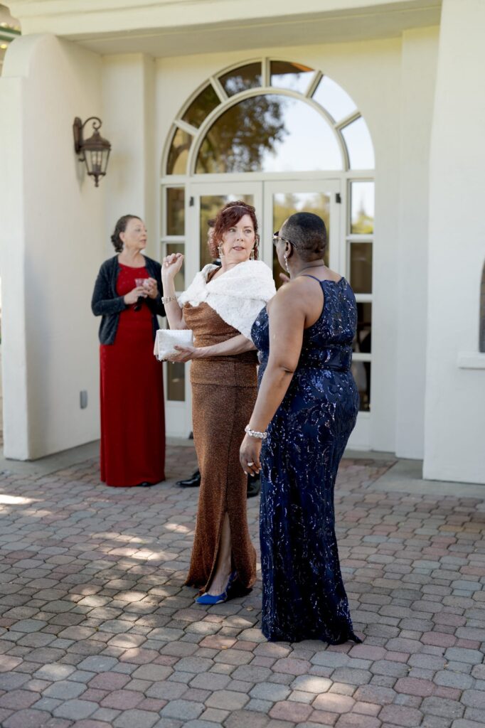 Female guests at the wedding cocktail hour talk to each other.