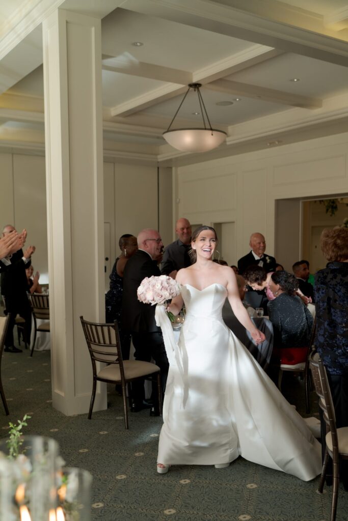 Bride in her wedding gown carries a big bouquet of flowers and walks into the reception party venue.