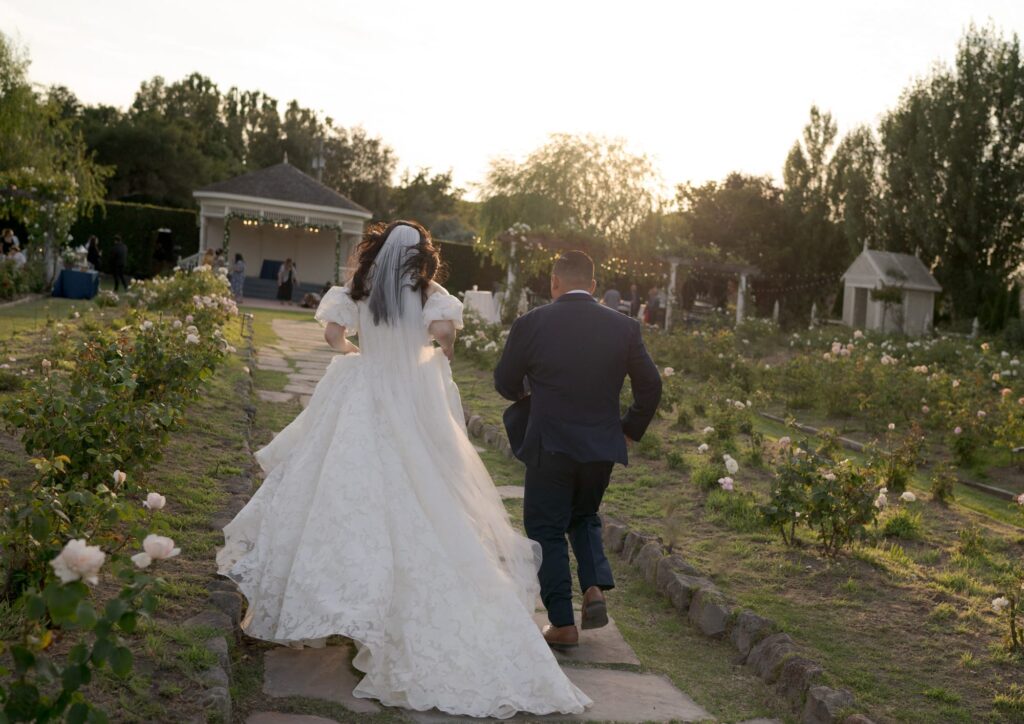 Bride and groom in wedding attires run towards the reception party venue.