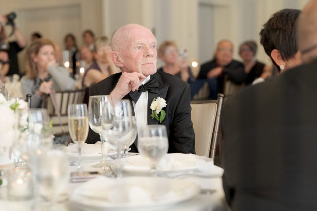 Father of the bride sits at a table and partakes in the reception party ceremonies.