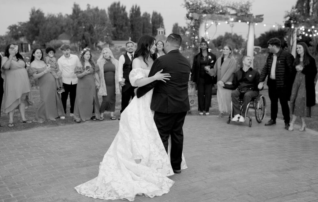 Newly married couple dance passionately at their reception party while guests watch from behind in awe.