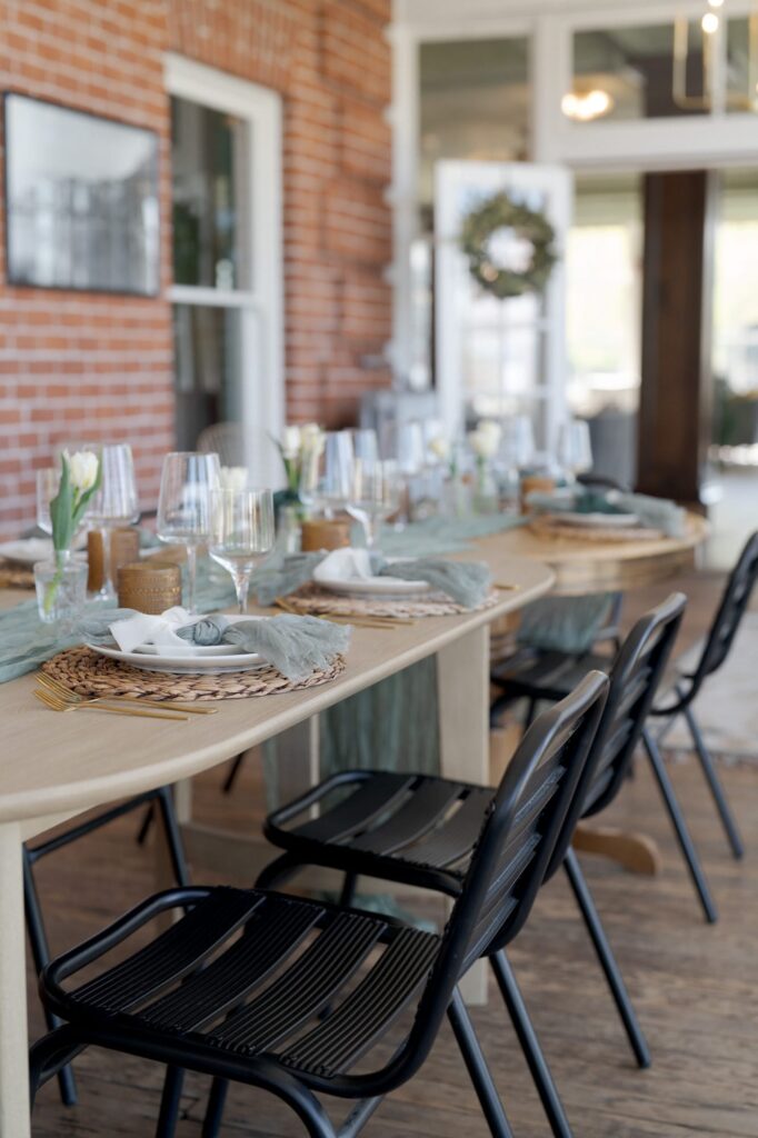 Black metal chairs and wooden tables with cutlery and wine glasses arrangement.