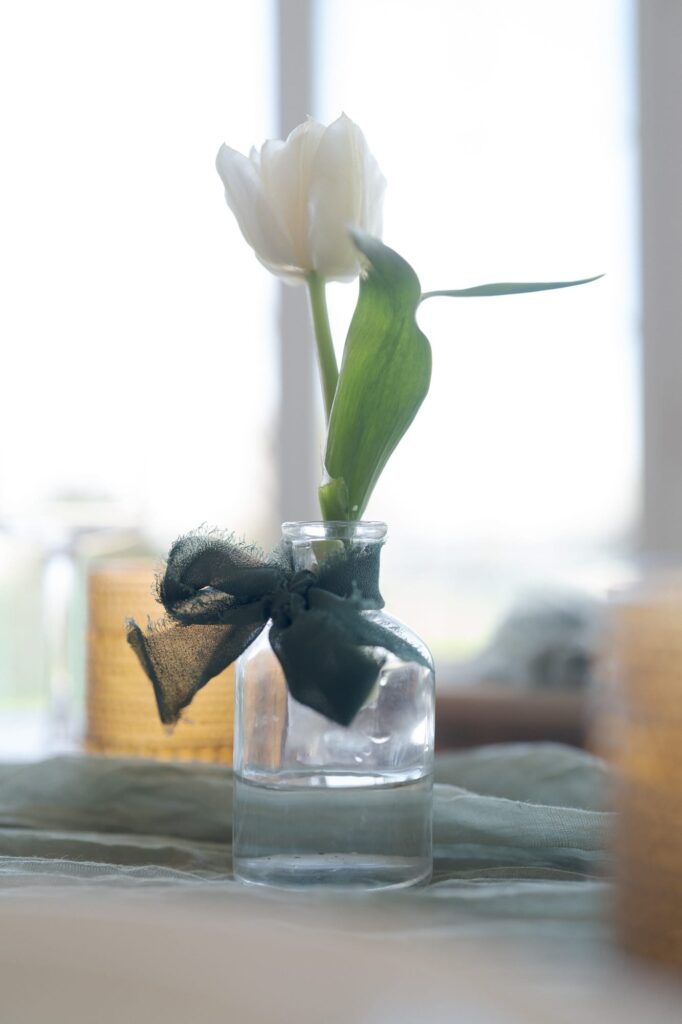 Freshly cut white flower with green leaves placed on a glass container half-filled with water as an aesthetic centerpiece.